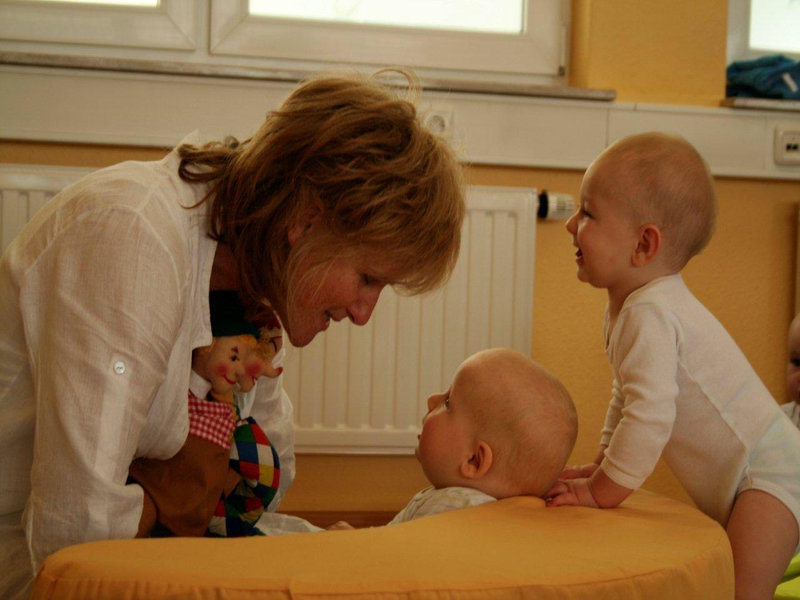 Kursleiterin spielt mit einer Handpuppe mit zwei Babys auf einem Wickelkissen
