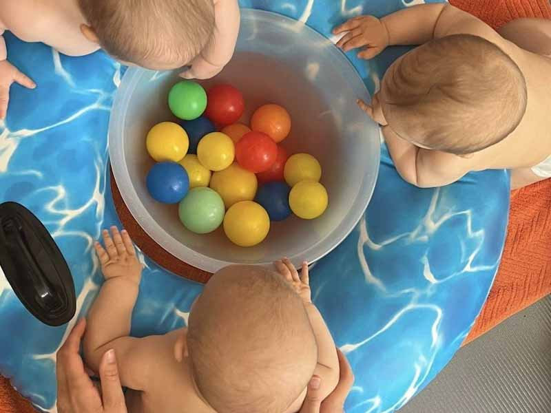 Babys greifen von oben in eine Schüssel mit bunten Bällen auf einer Poolmatte