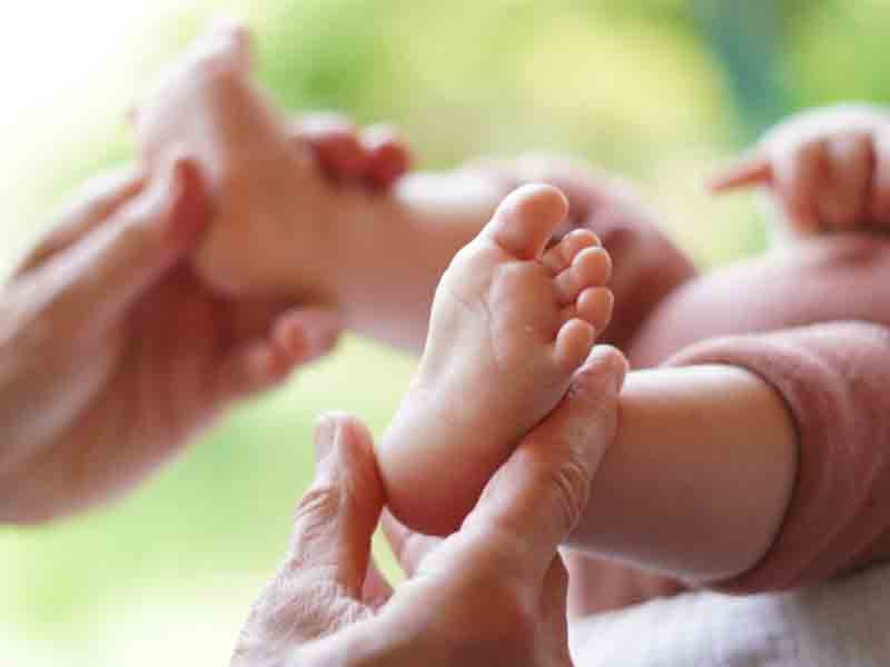 Erwachsene Hände massieren die Füße eines Babys, das auf dem Rücken liegt