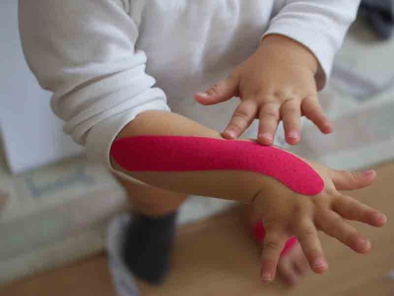 Kinderarm mit pinkfarbenem Kinesiotape entlang des Unterarms beklebt