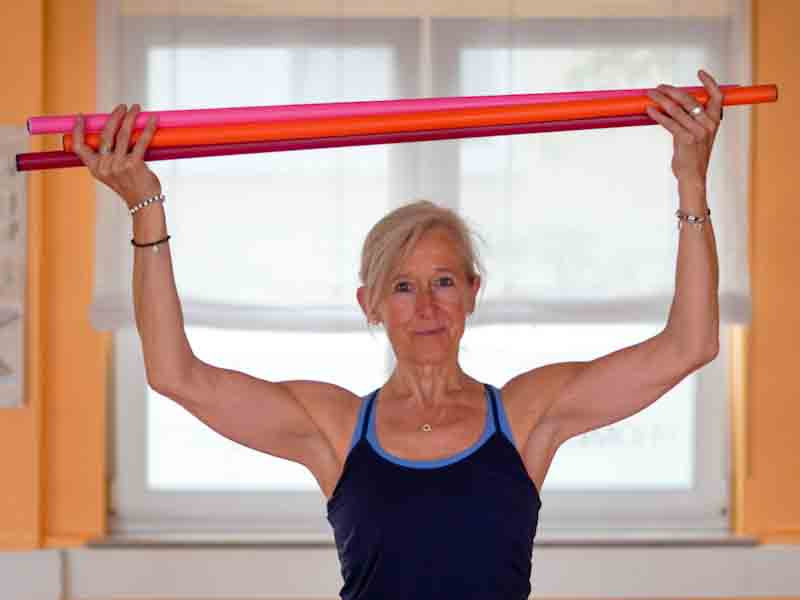 Frau hält einen bunten Gymnastikstab mit beiden Händen über dem Kopf